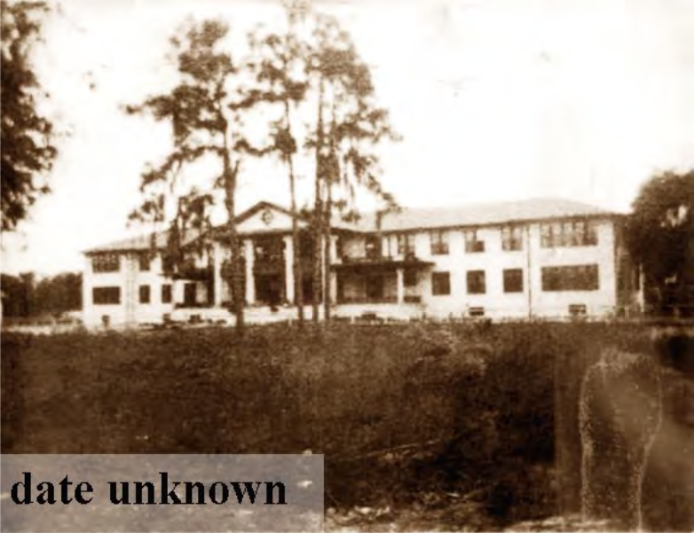 An old, sepia-toned photograph of a large, two-story building surrounded by trees, labeled with 'date unknown'.
