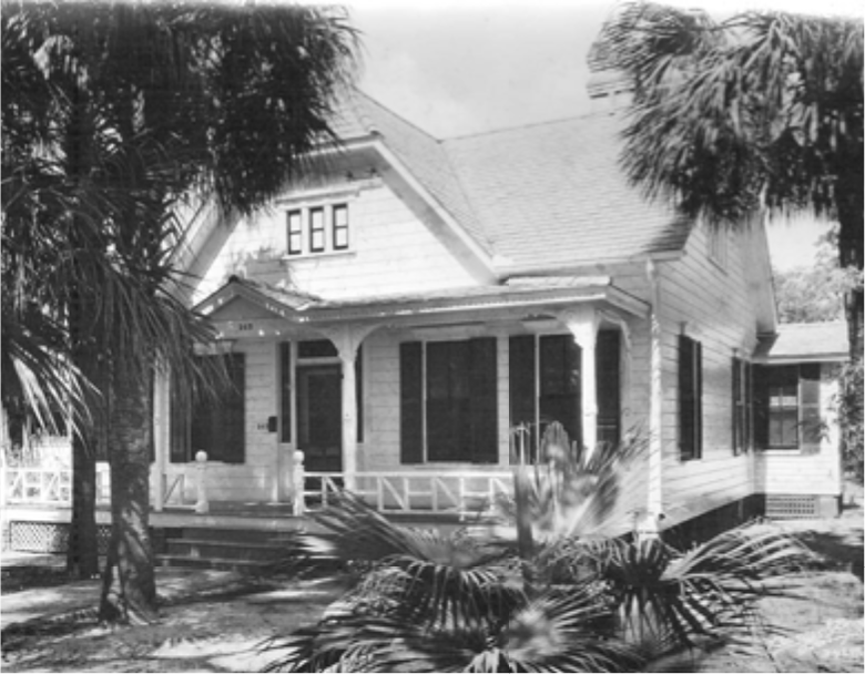 Black and white image of a Victorian-style house surrounded by palm trees.