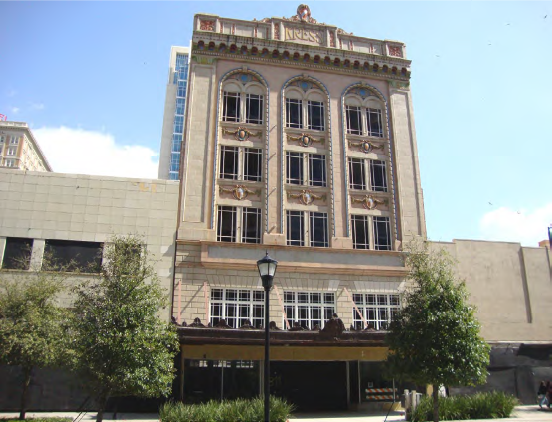 Historic building facade with arched windows and decorative elements, surrounded by greenery against a clear blue sky.