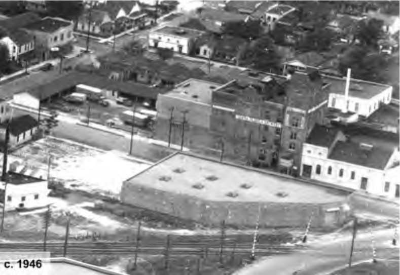 Aerial view of a city block featuring buildings, roads, and empty lots, captured around 1946.