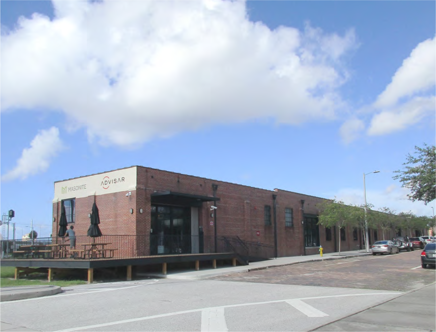 Exterior view of a brick building with outdoor seating, featuring signs for 'Wisonte' and 'Advisar,' under a partly cloudy sky.