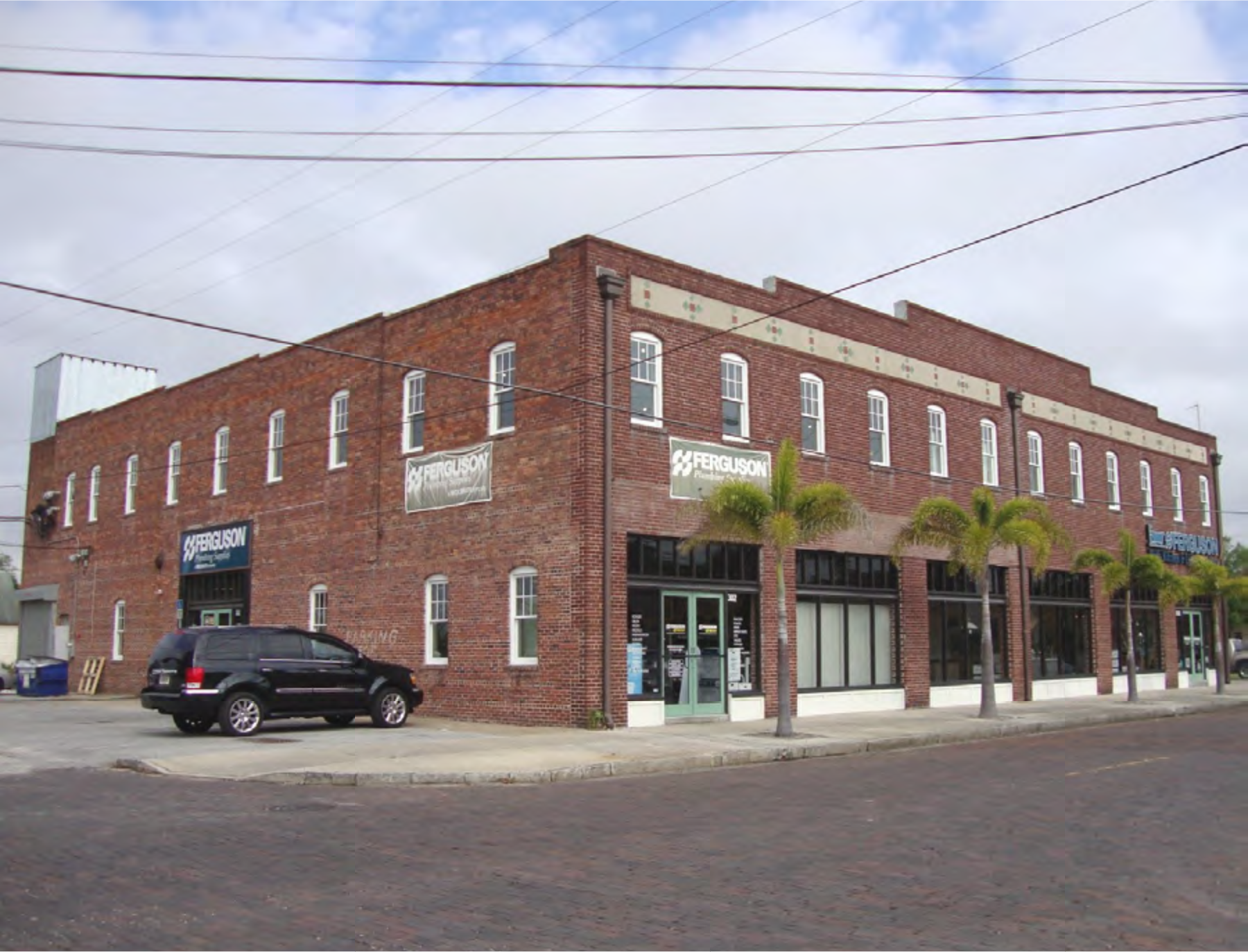 Brick building with windows and palm trees, featuring signage for Ferguson. A parked black SUV is visible in front.