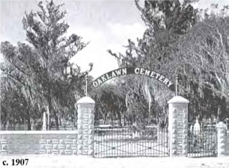 Black and white image of the entrance gate to Oaklawn Cemetery, surrounded by trees, dated circa 1907.
