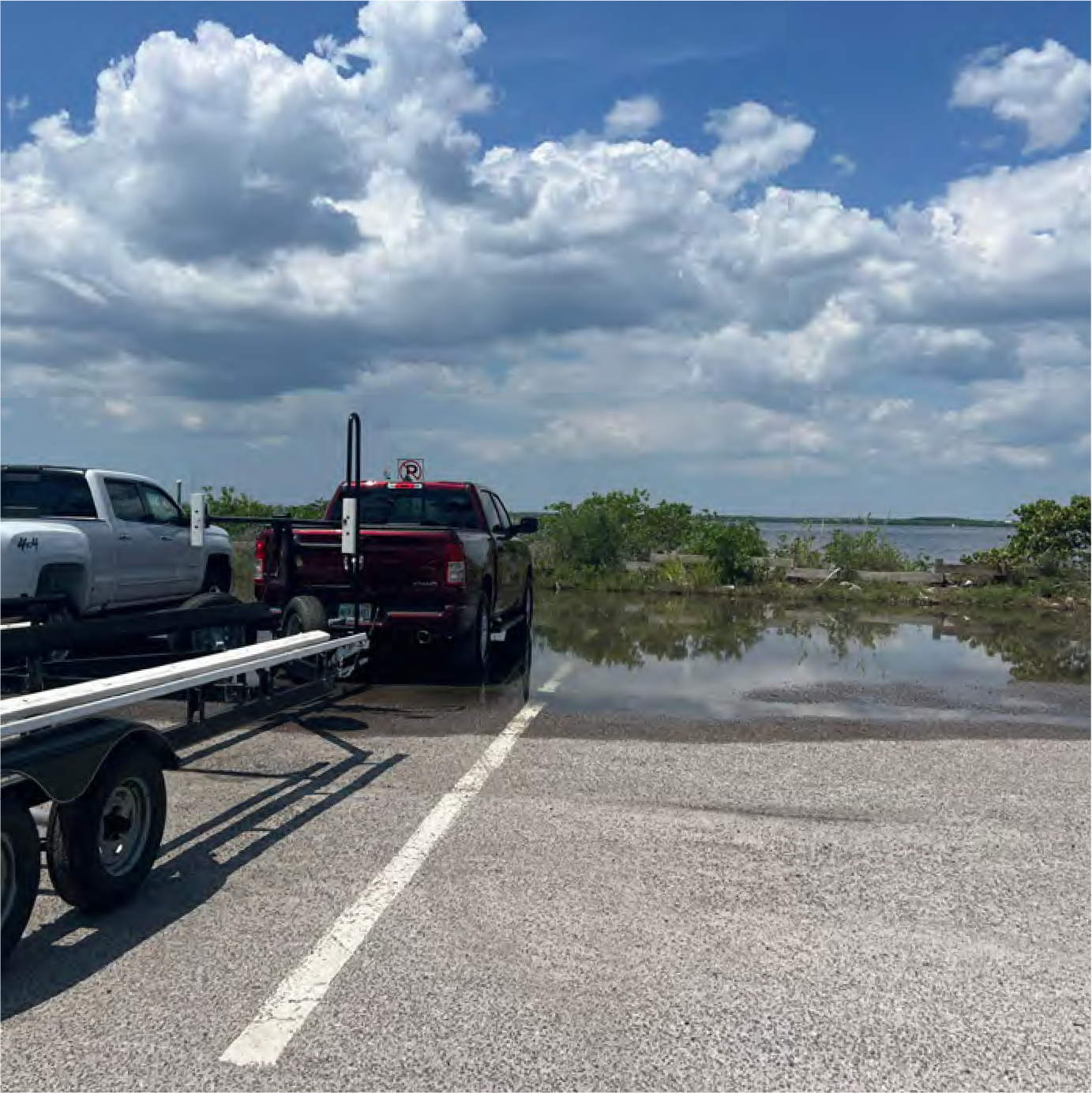 Parking area with trucks and a view of a flooded shoreline under a cloudy sky.