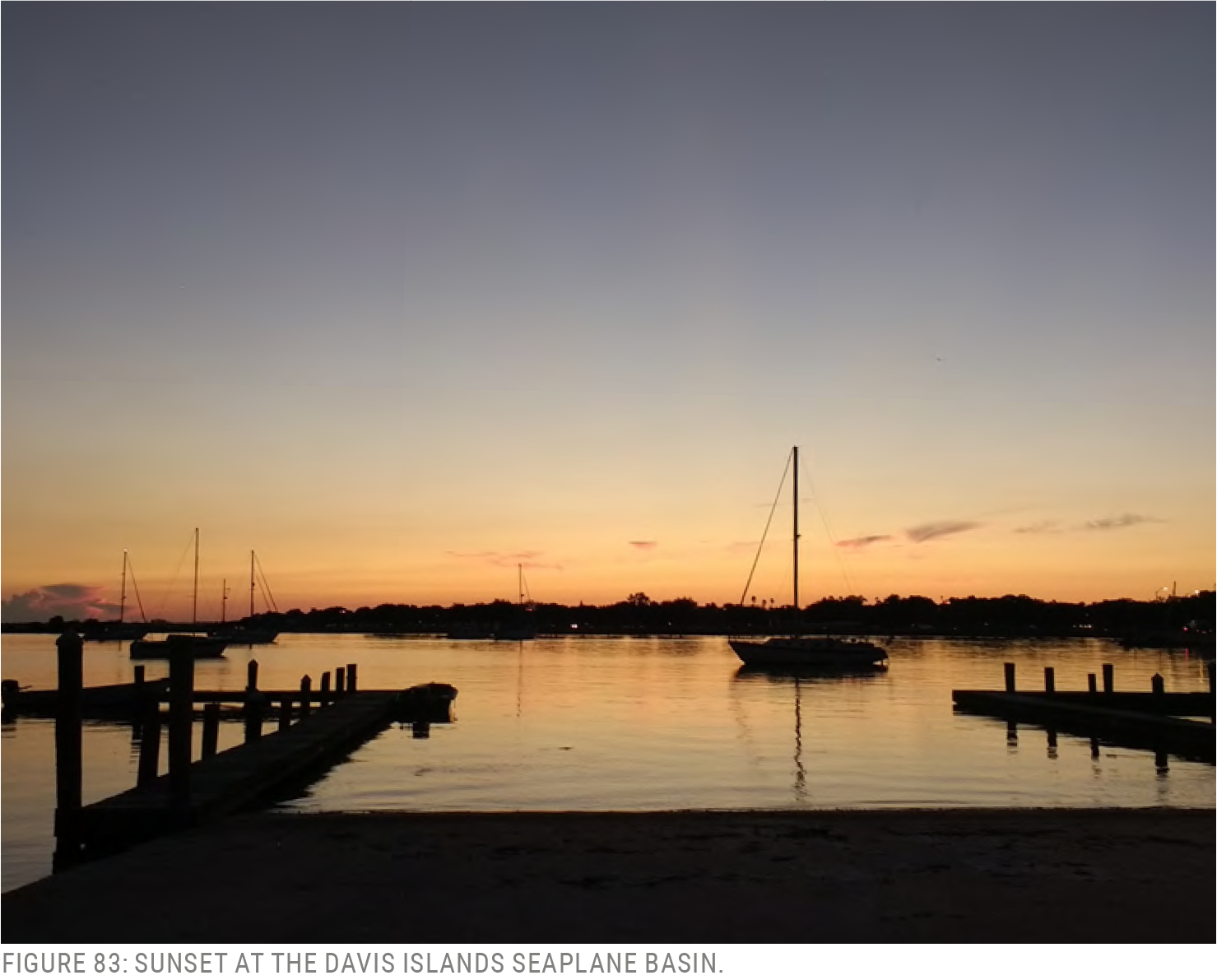 A serene sunset over the water at the Davis Islands seaplane basin, with moored boats silhouetted against the colorful sky.