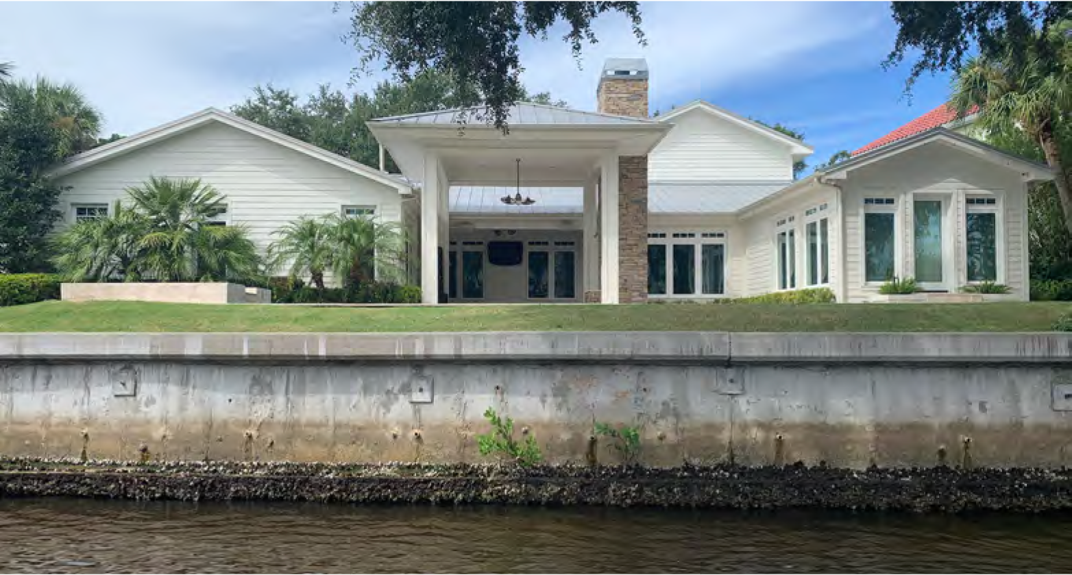 A modern house with a stone accent, large windows, and a landscaped yard, situated by a waterway.