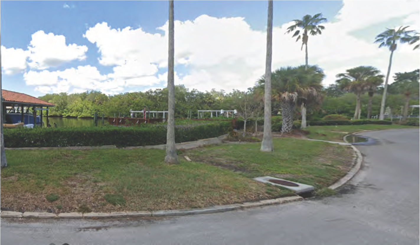 Scenic view of a serene waterfront with palm trees, a pathway, and greenery under a partly cloudy sky.