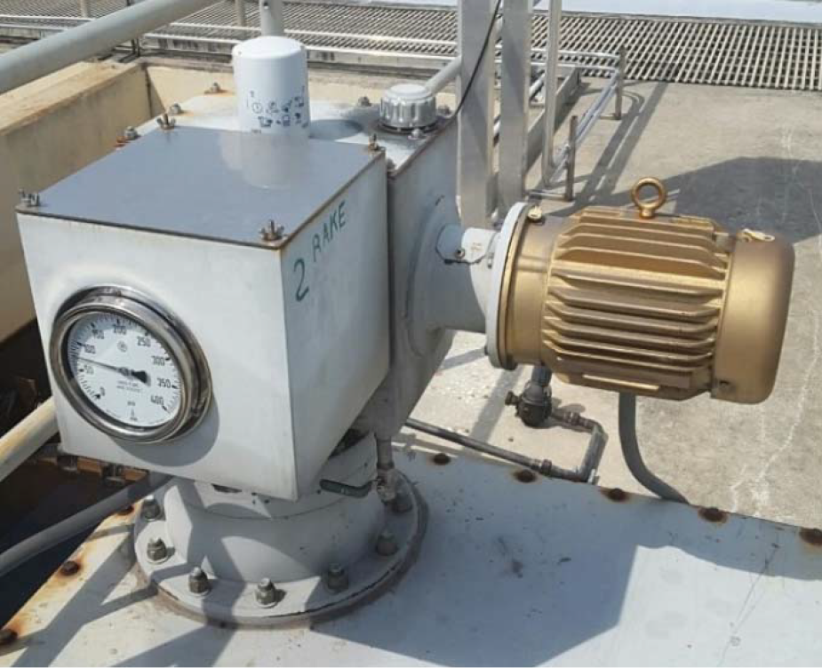 A close-up of a mechanical device featuring a pressure gauge and a motor, mounted on a metal surface with pipes.