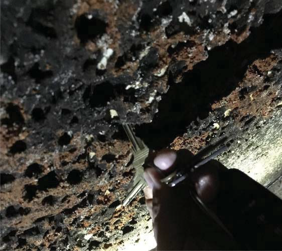 Close-up of a hand holding a tool, inspecting a corroded, textured surface with numerous holes and rust.