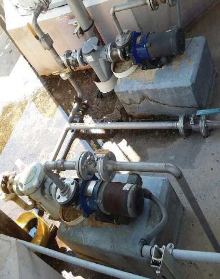 Industrial water pumps on concrete bases, connected by pipes, with some water pooling nearby.