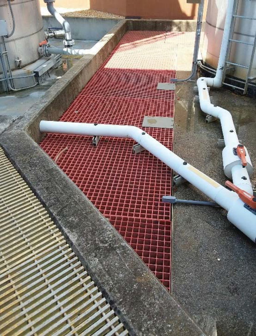 A rooftop surface with red grating, white pipes, and industrial equipment in the background.