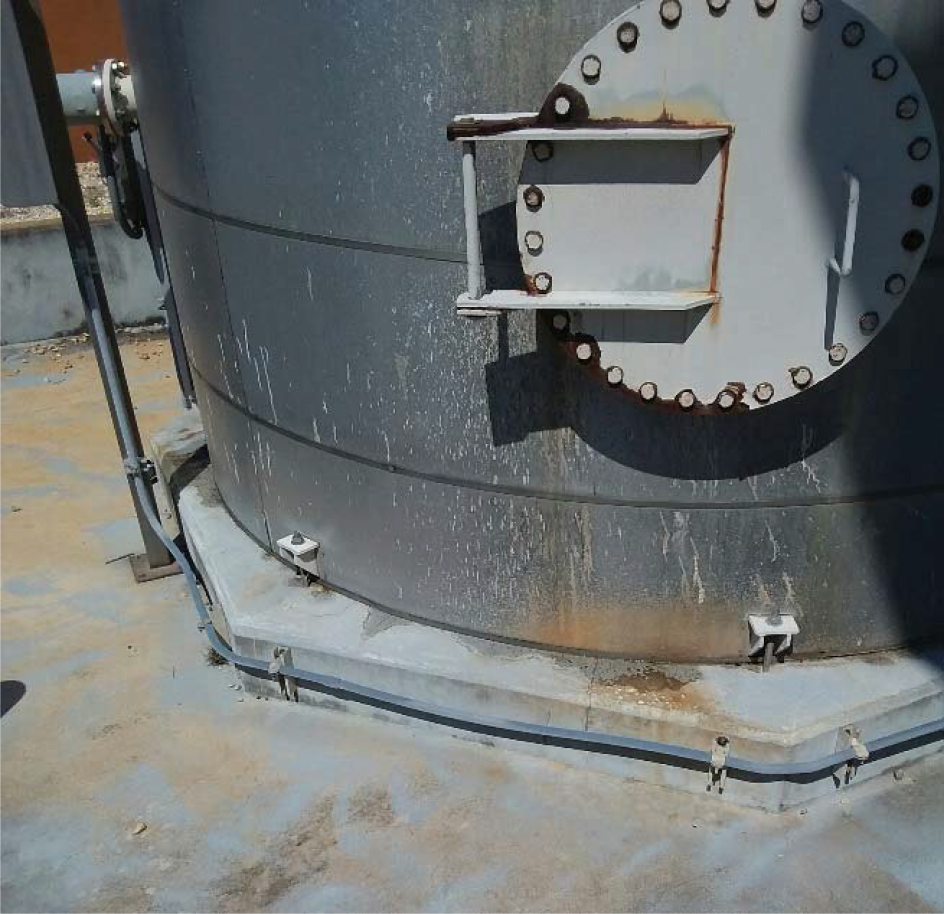 Weathered metal storage tank with visible rust and grime, situated on a concrete surface.