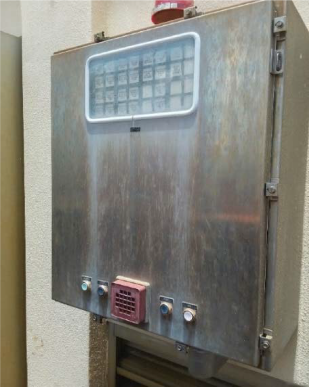 Metal control panel mounted on a wall, featuring buttons and a grid-like window.