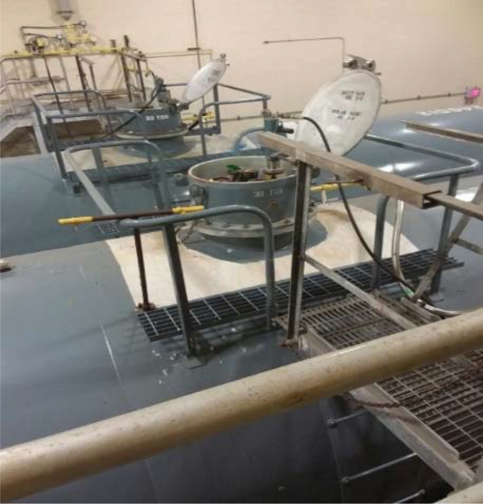 Industrial storage tanks with access hatches, pipes, and safety railings in a factory setting.