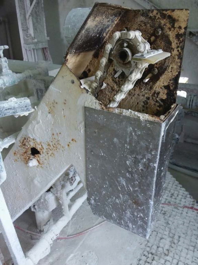 Corroded industrial machine component showing rust and buildup, with a chain mechanism visible inside.