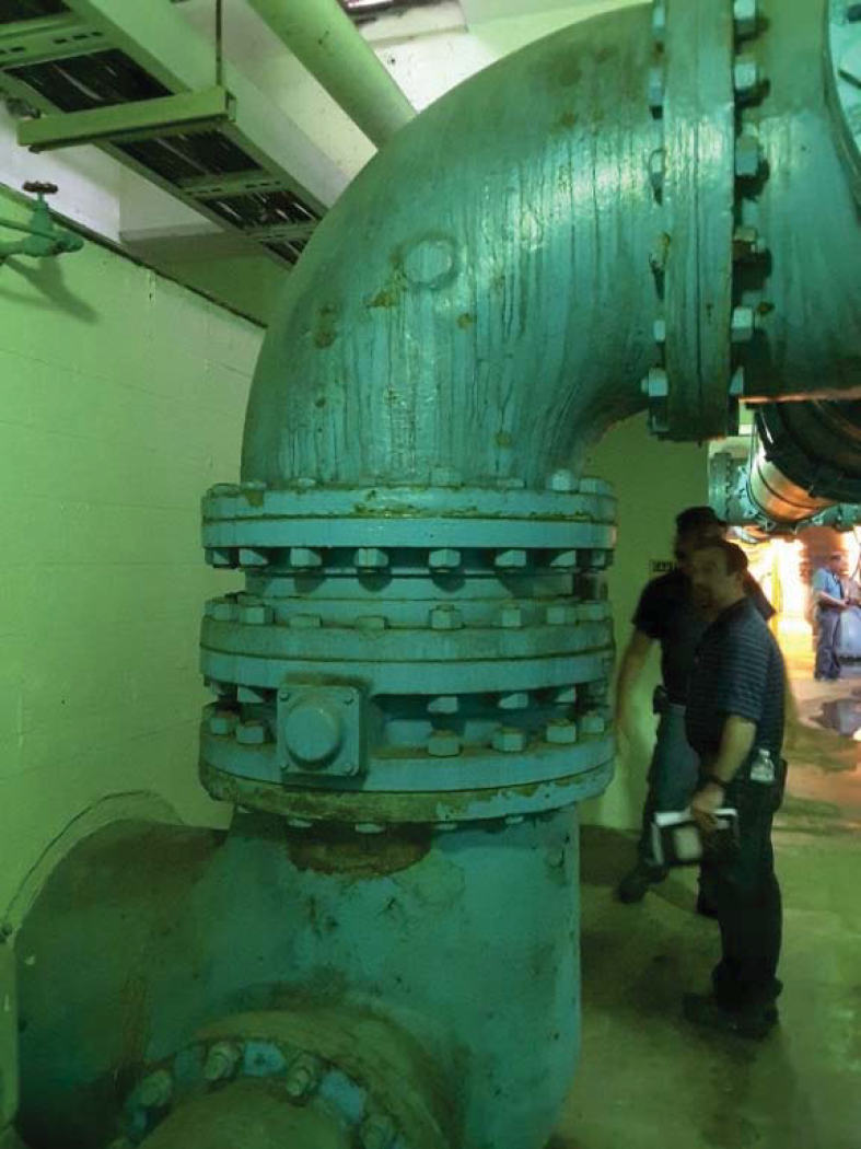 Large blue industrial pipes with a valve in a dimly lit underground setting.