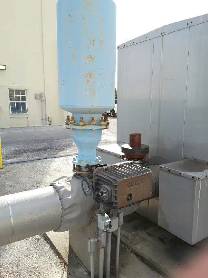 Industrial equipment featuring a large blue tank atop a pump and piping system against a building backdrop.