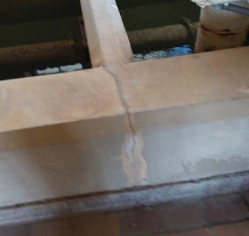 Concrete structure with a water channel and exposed pipes, showing wear and signs of age.