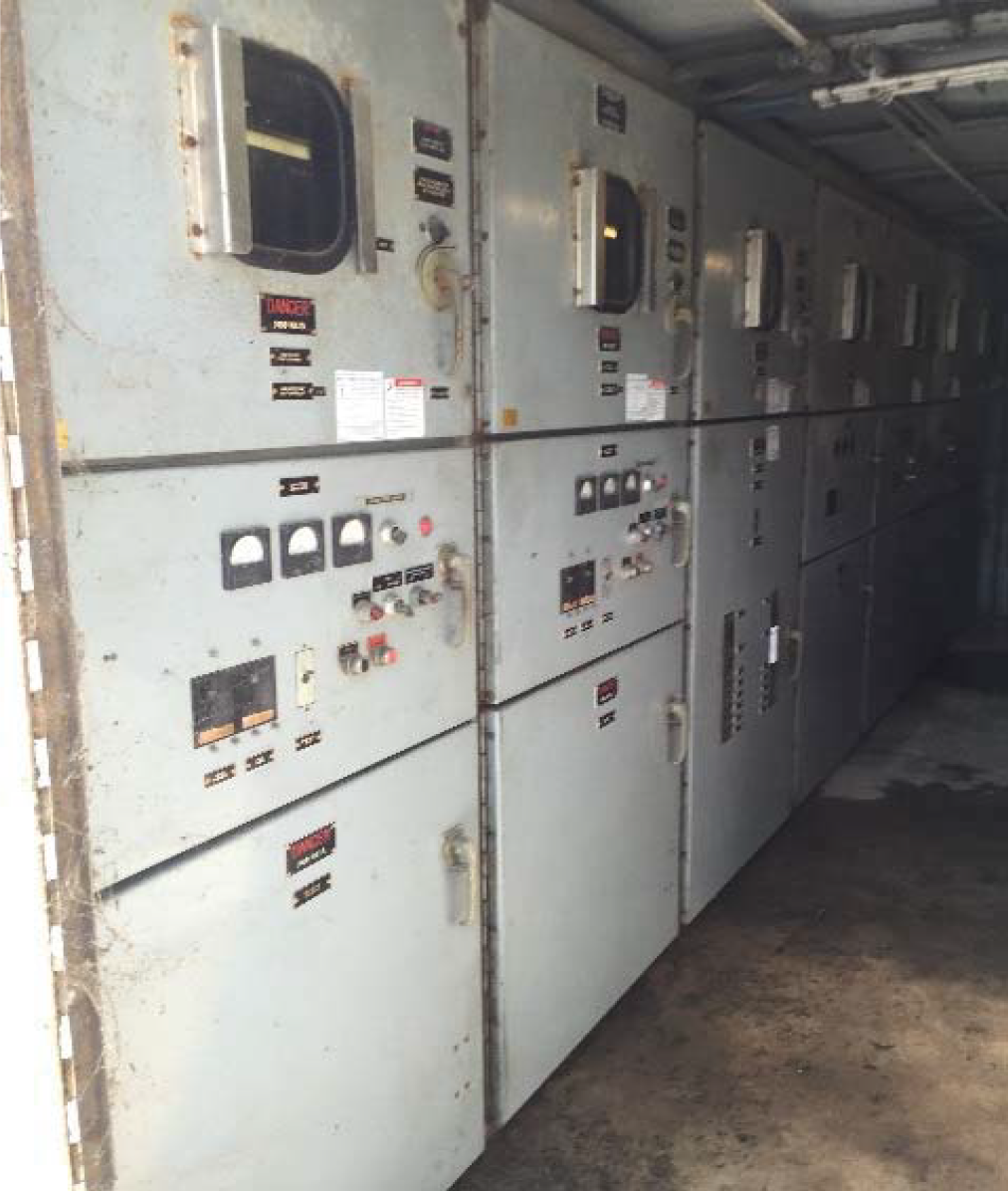 Wall of industrial control panels with various gauges, switches, and labels inside a factory or equipment room.