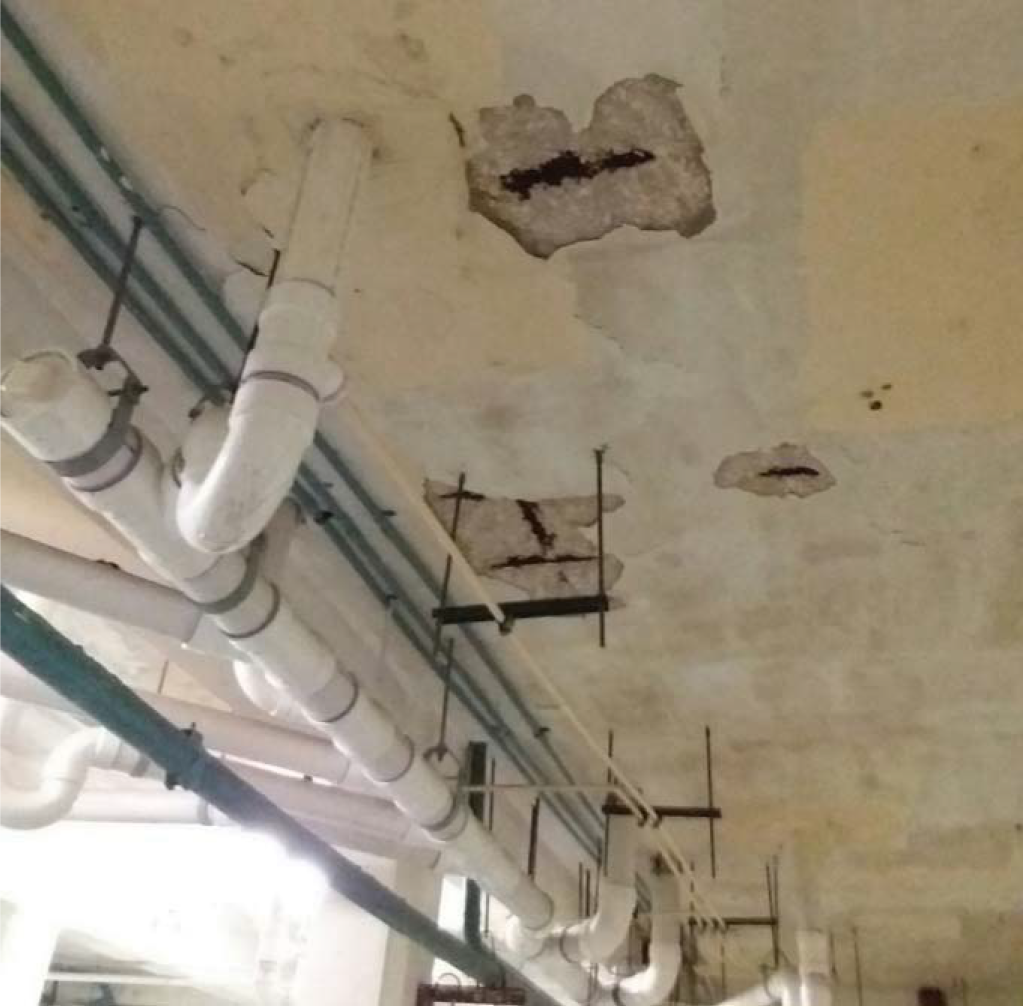 Ceiling with visible water damage, cracks, and exposed pipes in a building.
