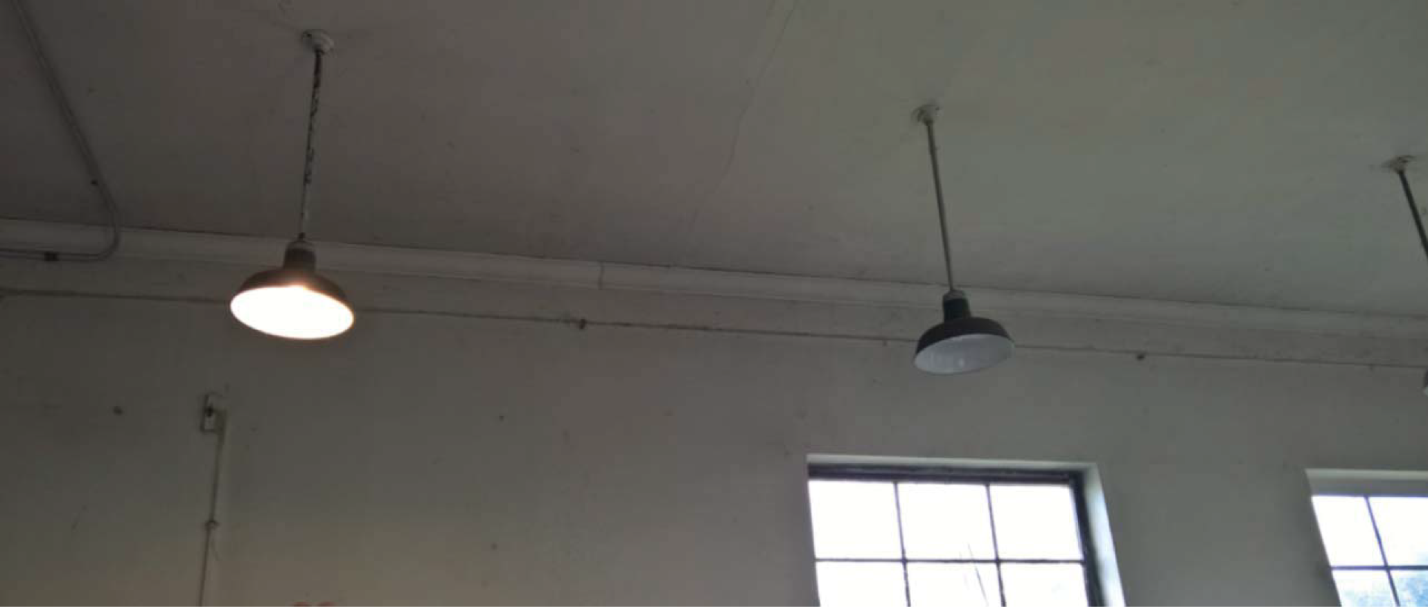 Two pendant lights hanging from a ceiling in a room with white walls and windows.