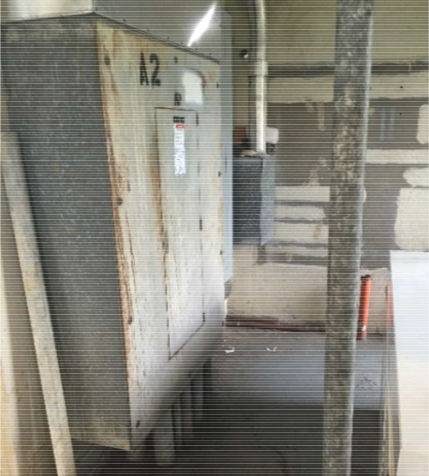 A weathered electrical box labeled 'A2' positioned against a wall in a partially finished room, with construction materials nearby.