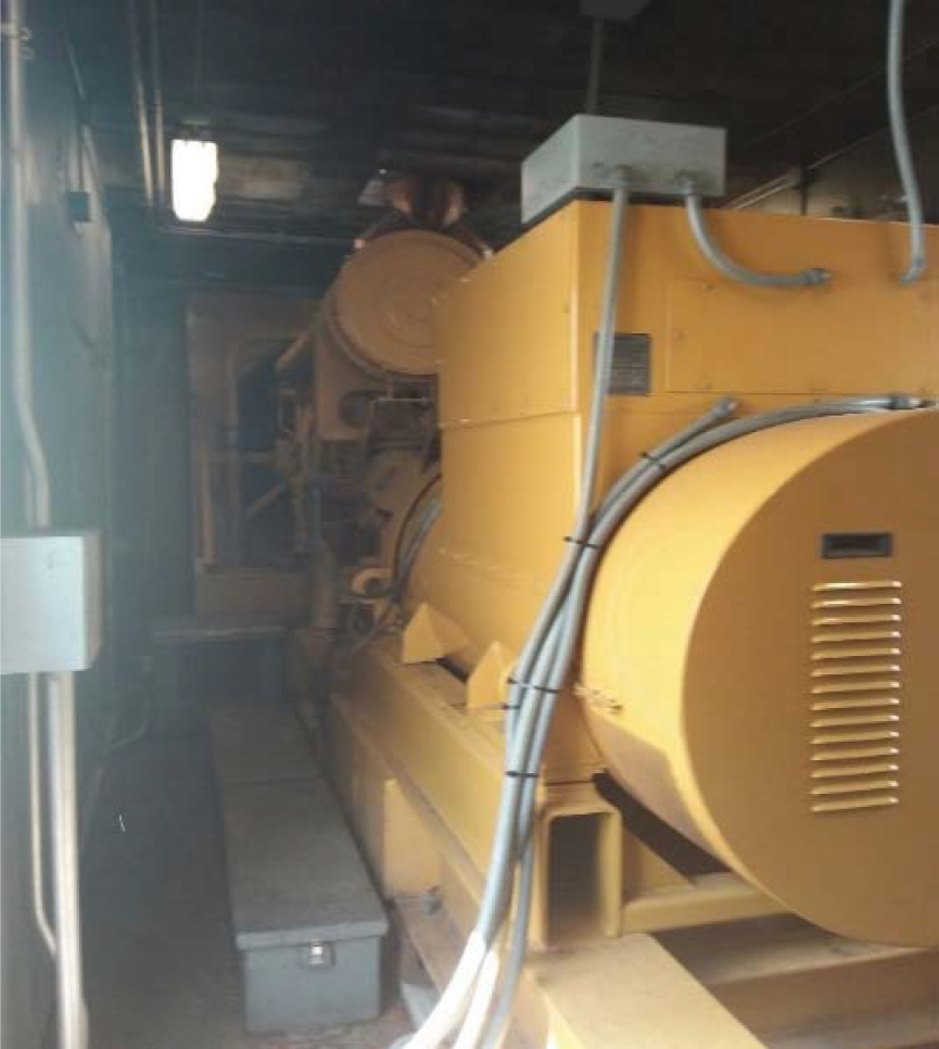 Industrial generator inside a dimly lit enclosure, featuring yellow casing and electrical cables.