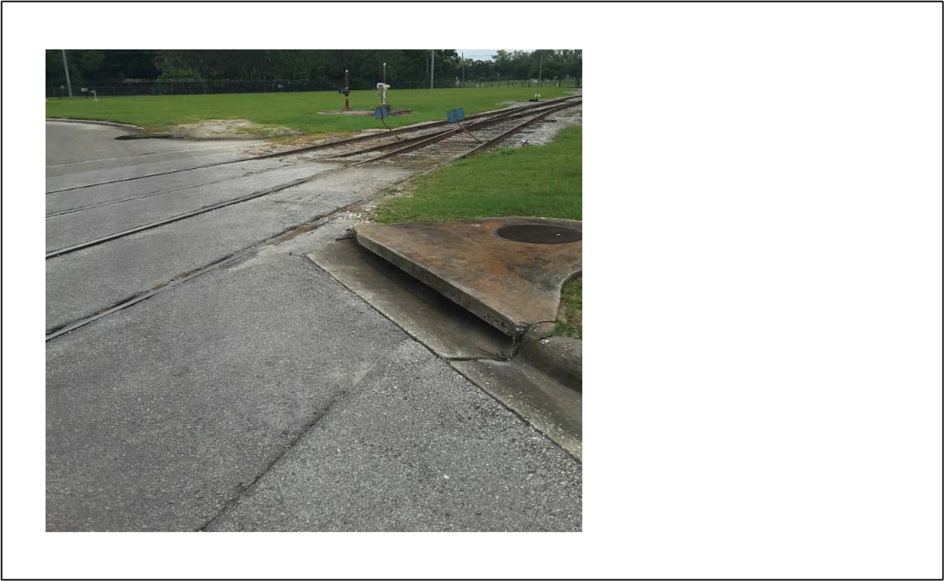 View of railway tracks on a concrete surface with grass and a lever signal in the background.