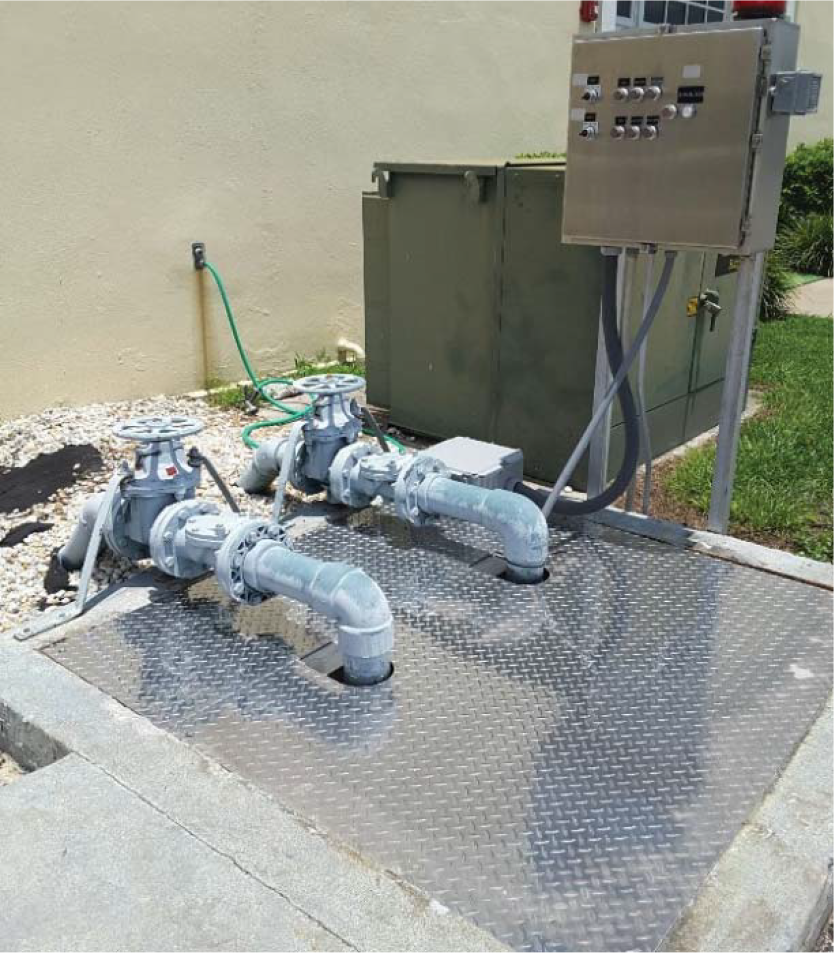 Two water pumps with piping on a metal platform, next to a control panel and utility box.