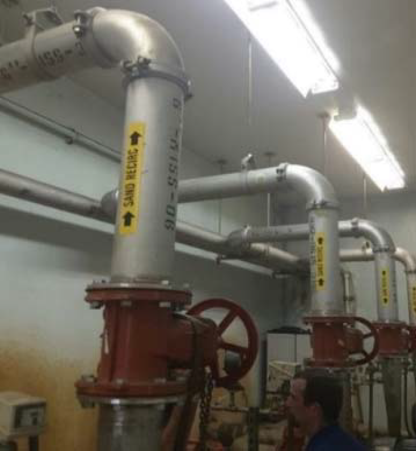 Industrial pipes and valves installed on walls, with visible labels and an operator nearby in a utility room.