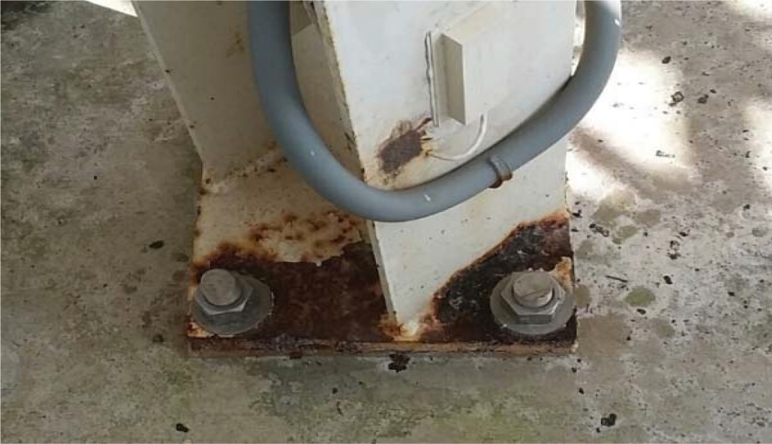 Metal base of a structure showing rust, two large bolts, and a gray electrical conduit.