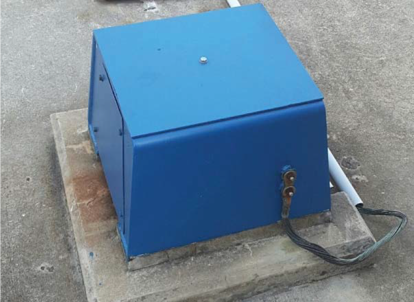 A blue, rectangular electrical box mounted on a concrete base, with a cable attached.