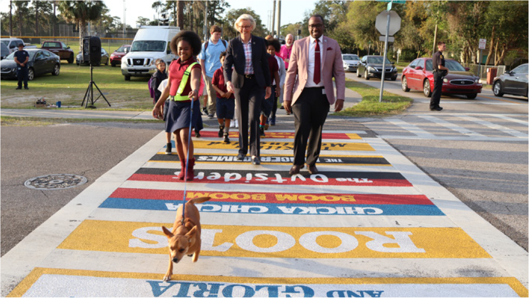 A group of people, including children in school uniforms, walking across a colorful crosswalk with a dog.
