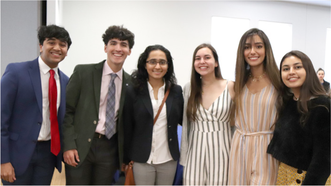 A group of six young people, smiling and posing together in a bright room.