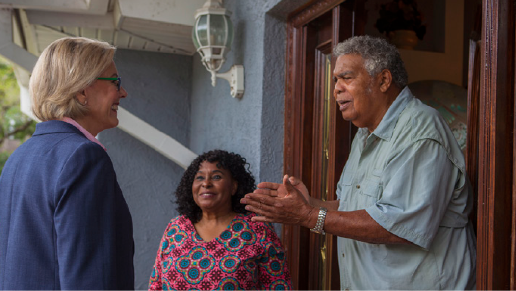 A woman in business attire converses with a couple at their home, smiling and engaged in a friendly discussion.