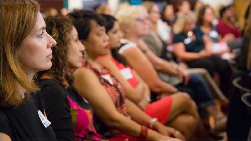 A group of women sitting in a conference or meeting setting, attentively listening.