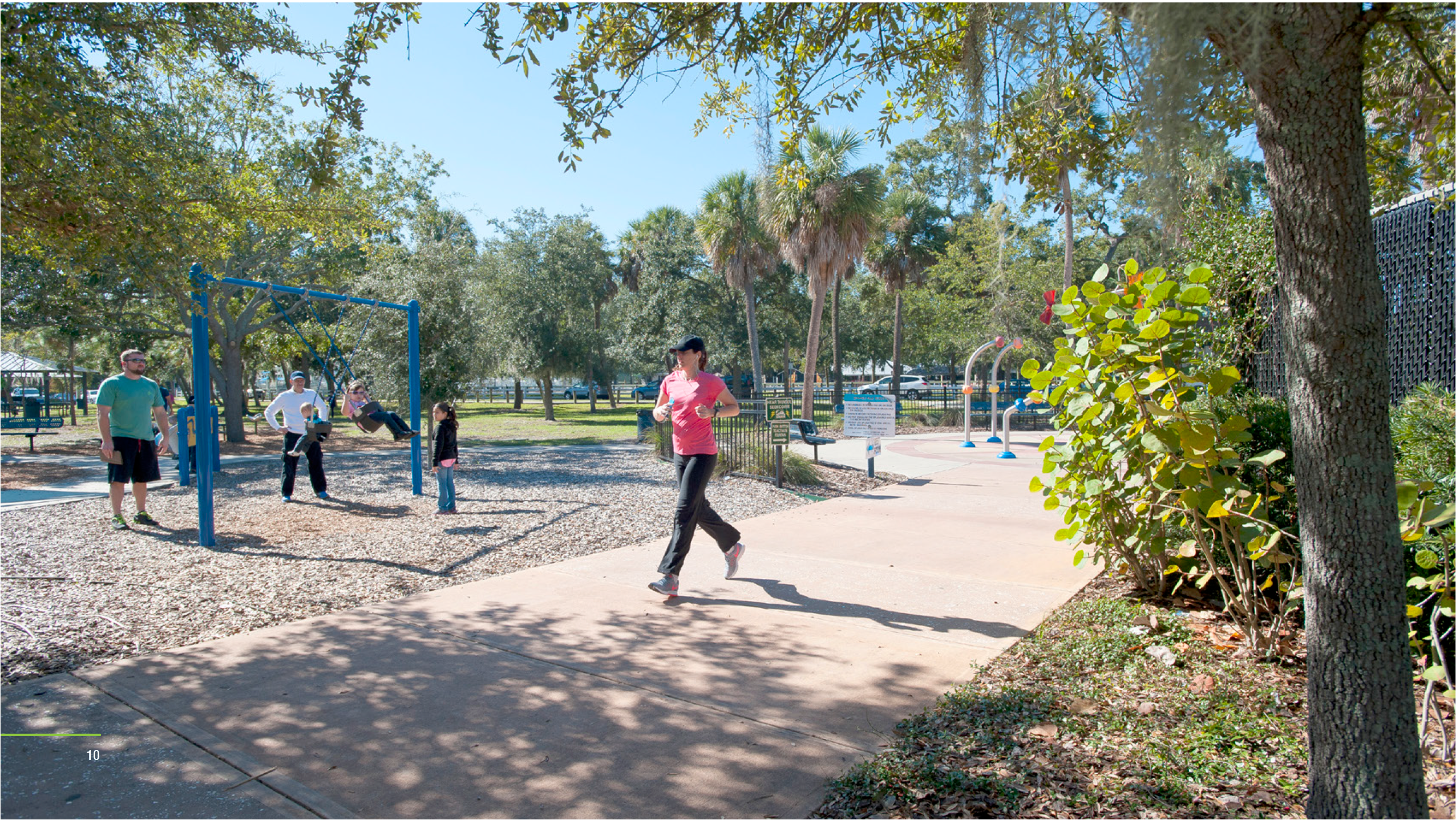 People exercising outdoors in a park with fitness equipment and shaded trees on a sunny day.