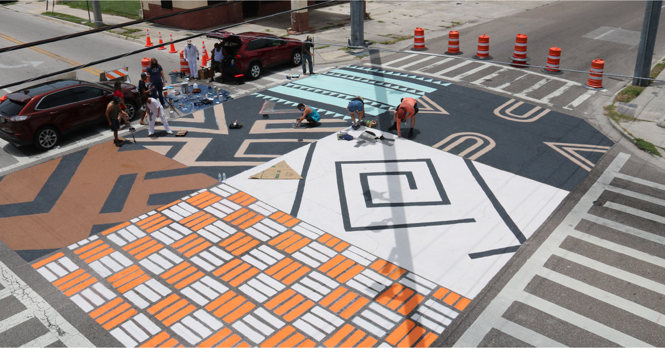 A group of people painting a colorful intersection mural featuring geometric patterns and vibrant colors.