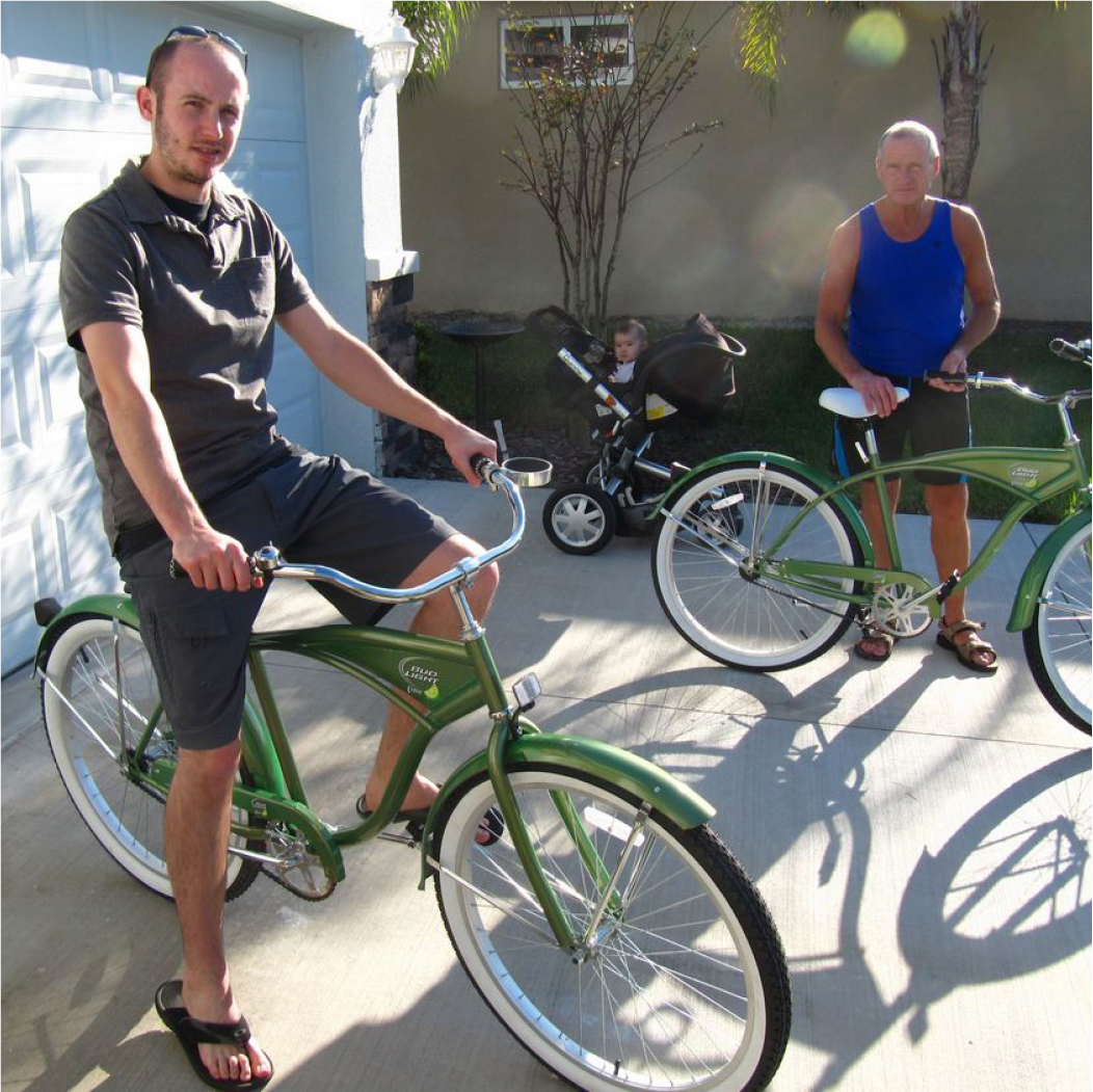 Two men by green bicycles in a driveway, with a stroller and a child in the background.