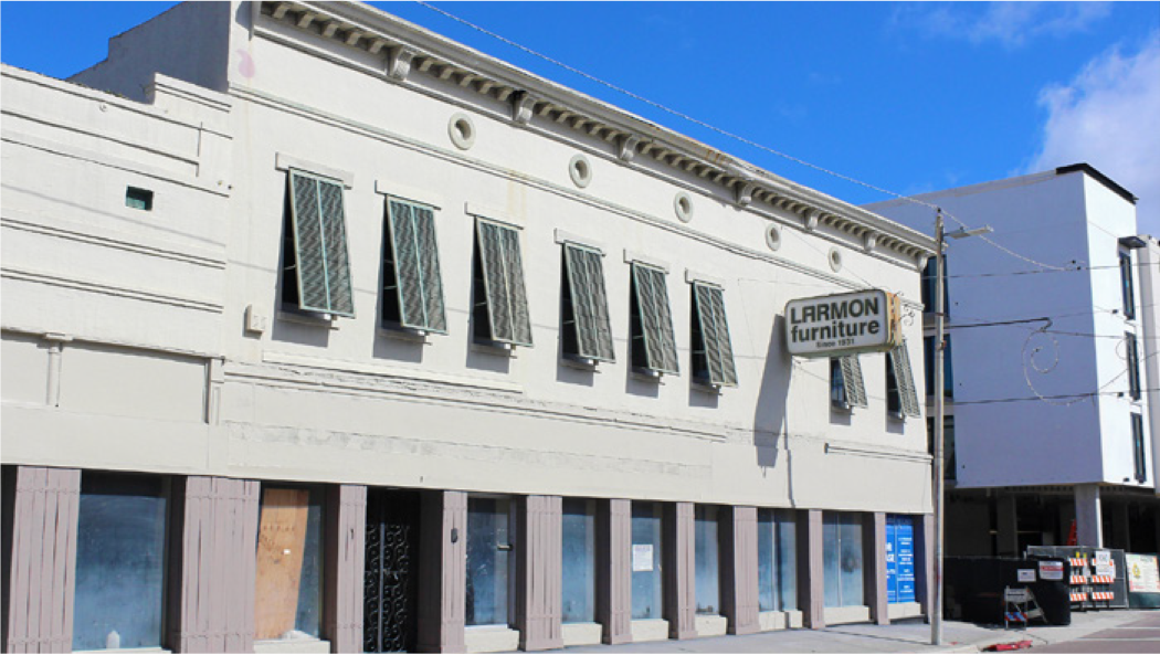 Exterior of Larmon Furniture building with boarded windows and decorative shutters, set against a clear blue sky.