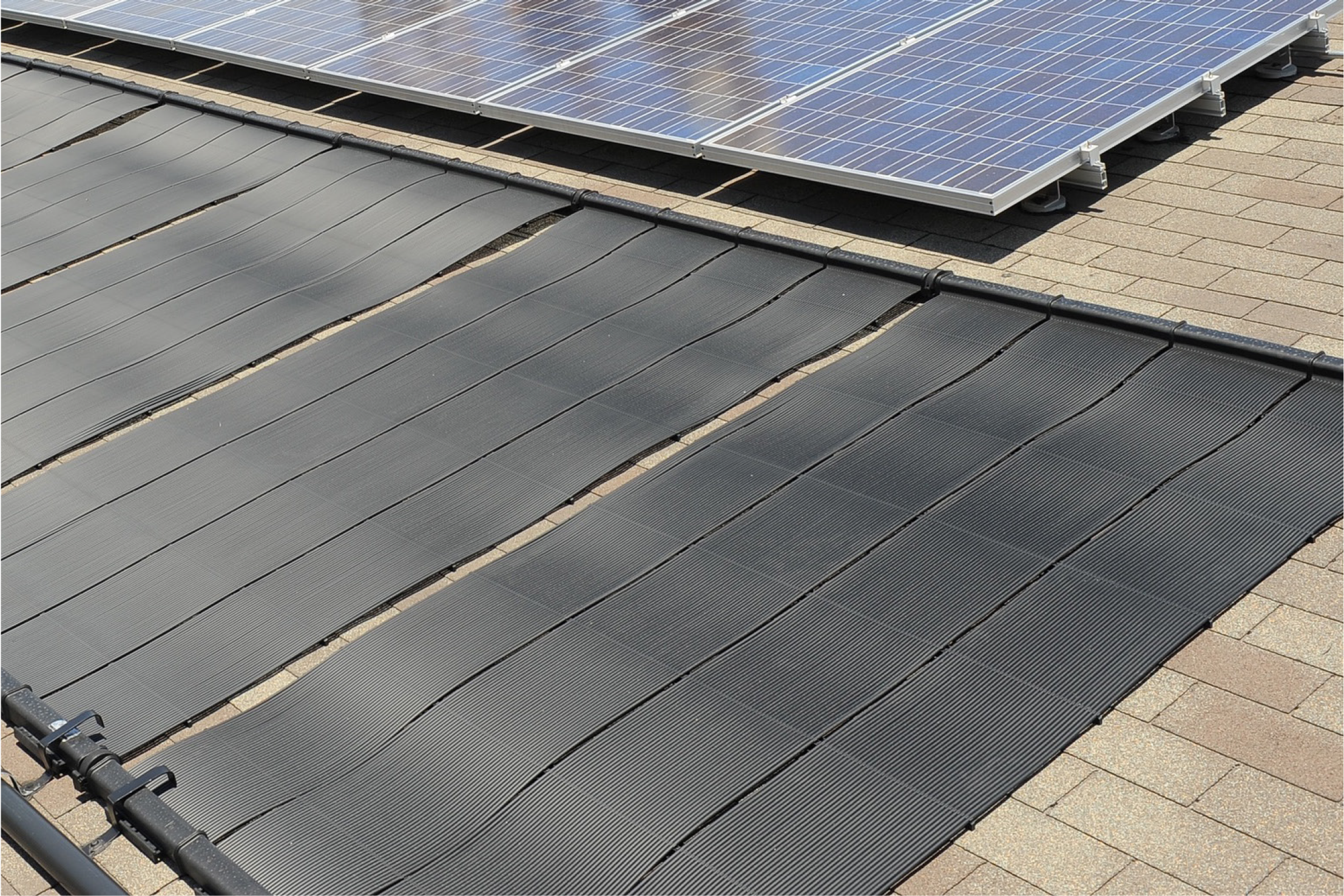 A rooftop showing solar panels and a black solar thermal collector system on a tiled surface.