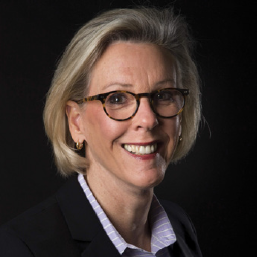 Professional portrait of a smiling woman with glasses and blonde hair, wearing a dark blazer and light shirt against a black background.