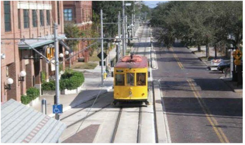 A yellow streetcar on tracks in a city street, with buildings and trees nearby.