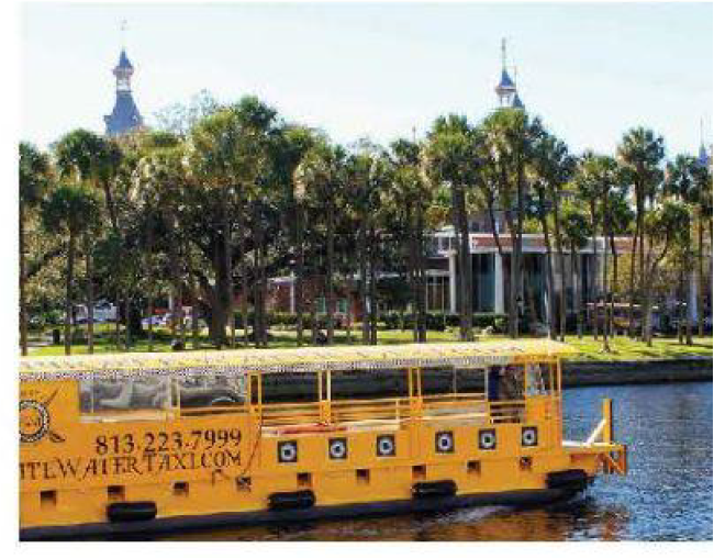 A yellow water taxi on a river with palm trees and buildings in the background.