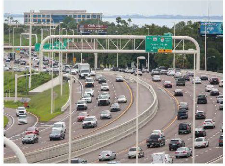 A busy highway with multiple lanes of traffic, vehicles moving in both directions, and a billboard in the background.