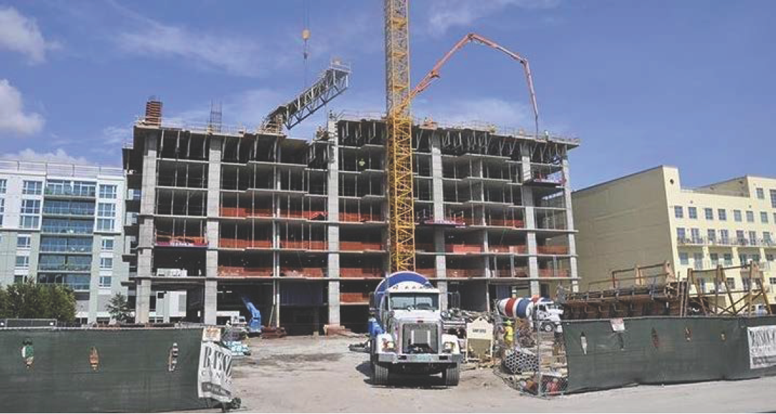 A construction site with a partially built multi-story building, a crane, and construction equipment on a clear day.