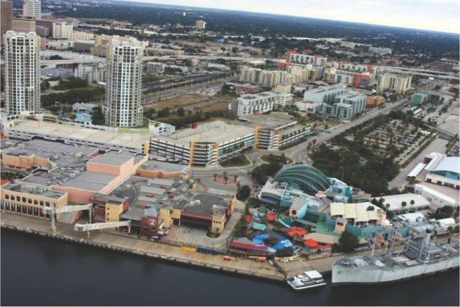 Aerial view of a waterfront urban area featuring buildings, parking lots, and a waterfront entertainment complex.