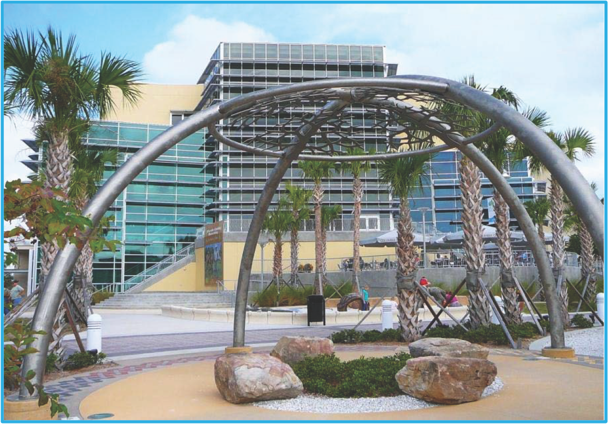 A modern sculpture in a park with palm trees and a glass building in the background.