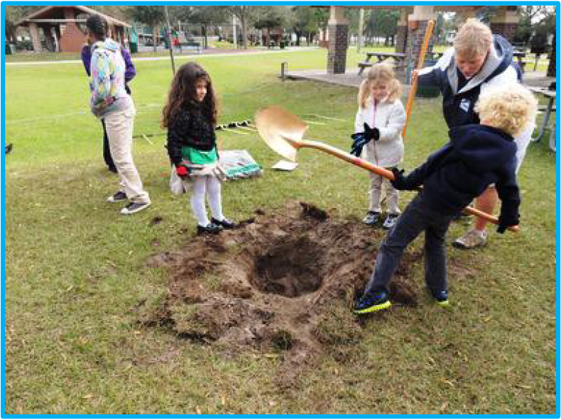 Children digging a large hole in the ground at a park, with an adult supervising.