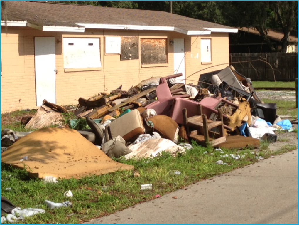 A large pile of discarded furniture and debris in front of a boarded-up building.